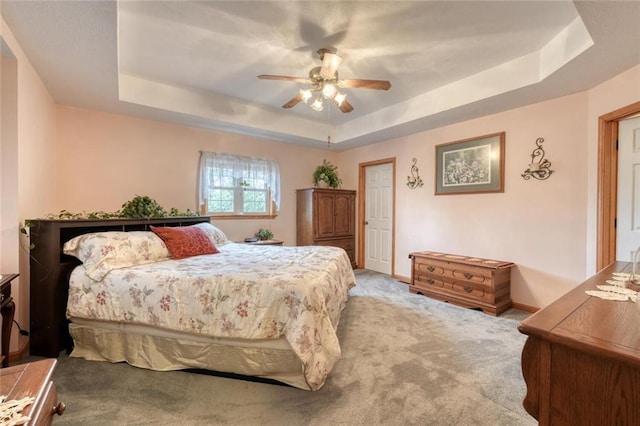 carpeted bedroom featuring baseboards, a ceiling fan, and a raised ceiling