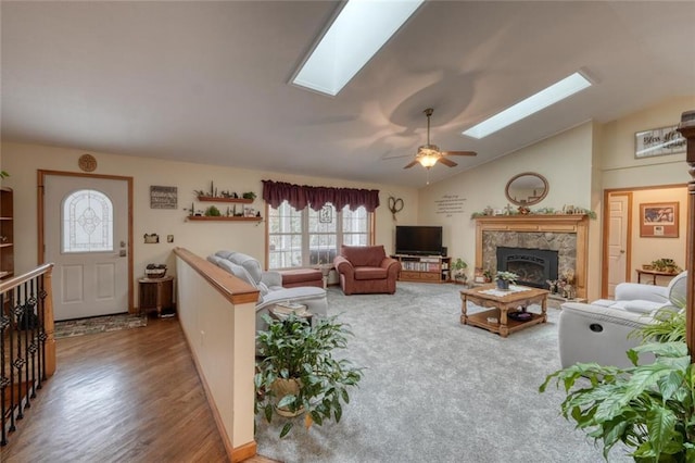 living area featuring a high end fireplace, wood finished floors, vaulted ceiling with skylight, and ceiling fan