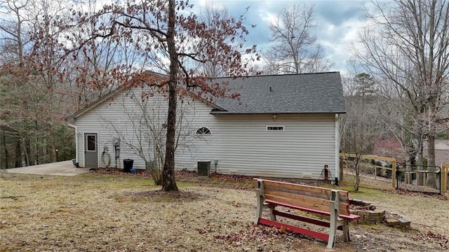 back of house featuring central air condition unit, a lawn, a shingled roof, and fence