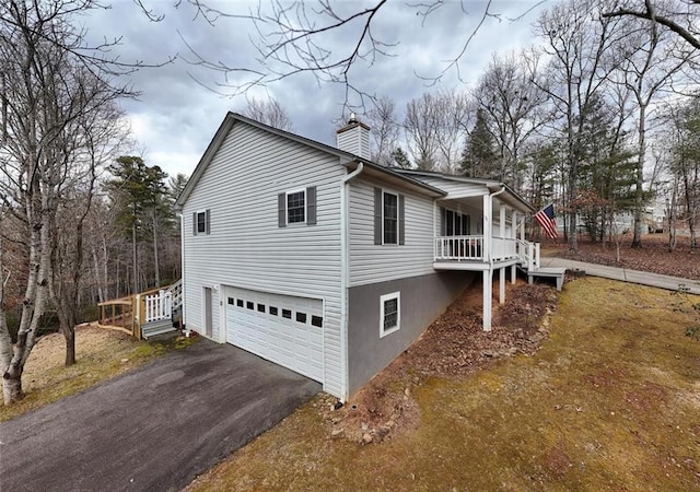 view of home's exterior featuring a chimney, covered porch, a garage, and aphalt driveway