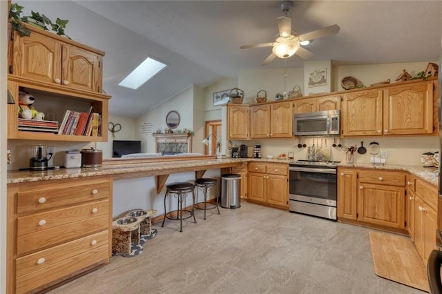 kitchen featuring a kitchen breakfast bar, stainless steel appliances, vaulted ceiling with skylight, a ceiling fan, and a fireplace