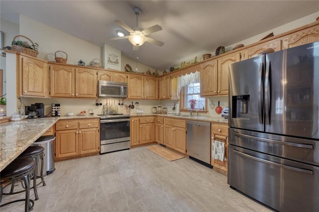 kitchen featuring vaulted ceiling, stainless steel appliances, a sink, ceiling fan, and light stone countertops