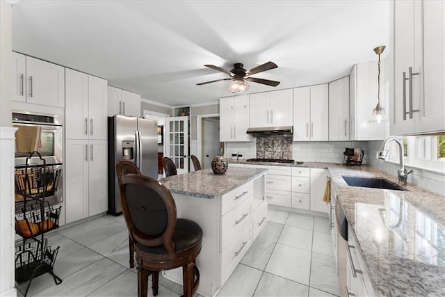 kitchen with sink, white cabinetry, hanging light fixtures, appliances with stainless steel finishes, and a kitchen breakfast bar