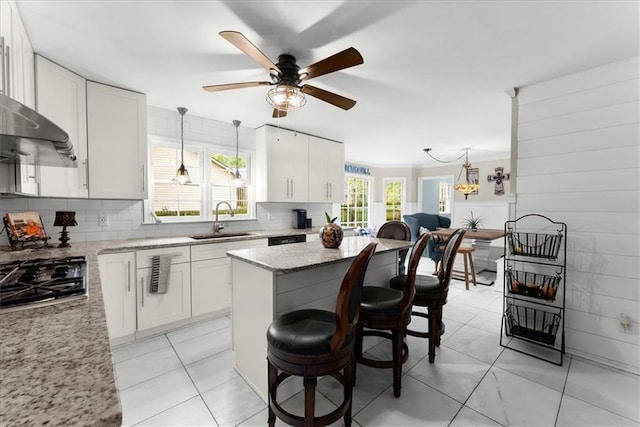 kitchen featuring pendant lighting, sink, white cabinets, stainless steel gas cooktop, and light stone counters