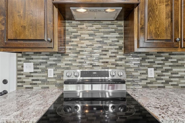 kitchen with stainless steel range with electric stovetop, wall chimney range hood, light stone countertops, and decorative backsplash