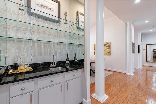 bar with decorative columns, light wood-style flooring, wet bar, a sink, and recessed lighting