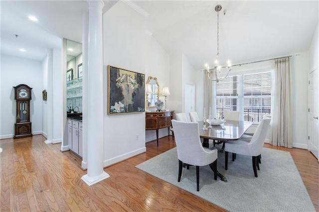dining space with a notable chandelier, lofted ceiling, light wood finished floors, and ornate columns