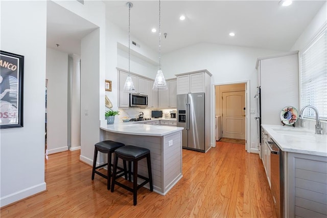 kitchen with light wood finished floors, a peninsula, stainless steel appliances, a kitchen bar, and a sink