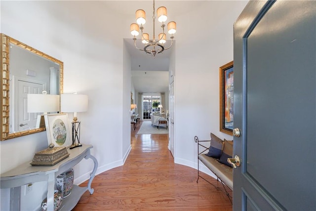 corridor with an inviting chandelier, wood finished floors, and baseboards