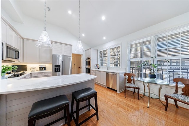kitchen featuring white cabinets, a peninsula, appliances with stainless steel finishes, light wood-style floors, and vaulted ceiling