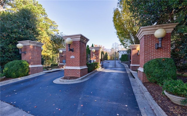 view of road featuring curbs, a gate, a gated entry, and street lights