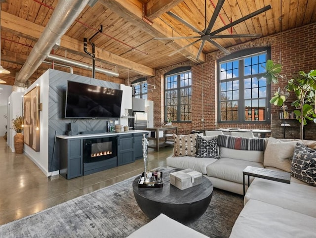 living area featuring ceiling fan, a glass covered fireplace, brick wall, wooden ceiling, and a towering ceiling