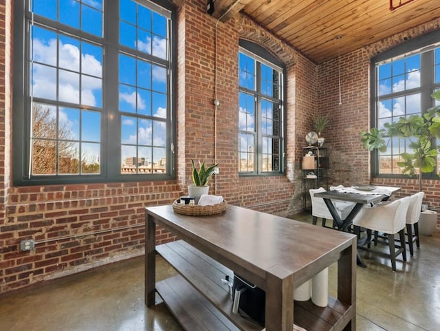 dining area with wooden ceiling, a high ceiling, brick wall, and finished concrete floors