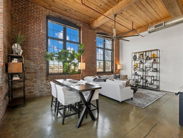 dining space with beam ceiling, wooden ceiling, brick wall, concrete flooring, and a towering ceiling