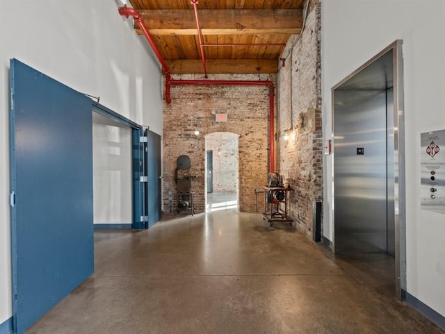 corridor featuring beamed ceiling, finished concrete floors, elevator, brick wall, and wood ceiling