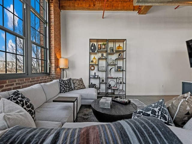 living room featuring beamed ceiling, brick wall, baseboards, and a towering ceiling