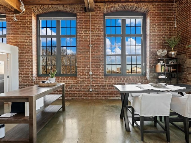 dining room with brick wall, finished concrete flooring, a towering ceiling, and a healthy amount of sunlight