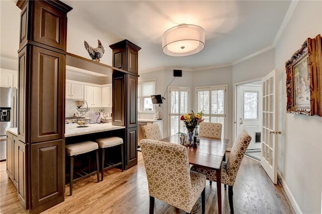 dining area with light wood-style floors, baseboards, and crown molding