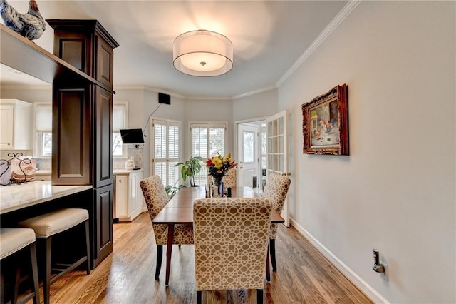 dining area featuring light wood-style floors, baseboards, and crown molding