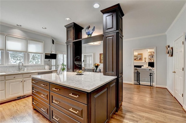 kitchen featuring a sink, white cabinetry, ornamental molding, light stone countertops, and light wood finished floors