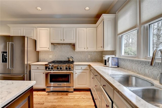 kitchen featuring high end appliances, white cabinetry, a sink, and light wood finished floors