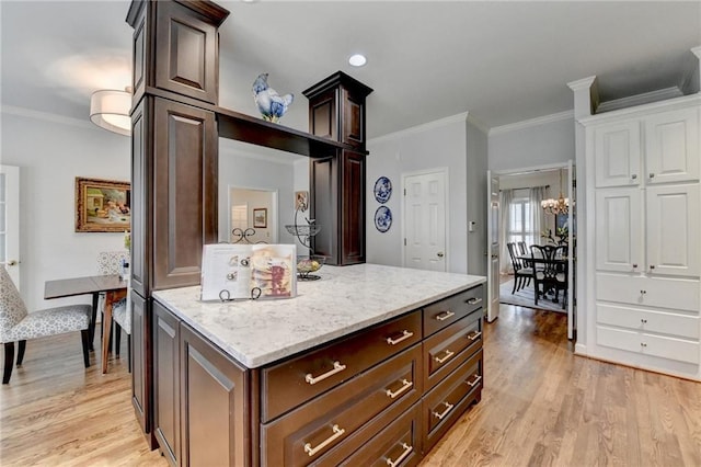 kitchen featuring dark brown cabinetry, a center island, light stone countertops, crown molding, and light wood-style floors