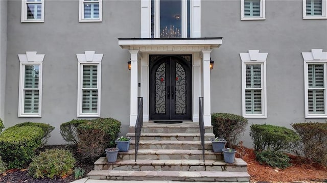 view of exterior entry featuring french doors, visible vents, and stucco siding