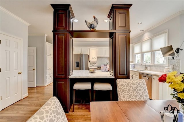 kitchen featuring a sink, appliances with stainless steel finishes, decorative backsplash, a kitchen bar, and crown molding