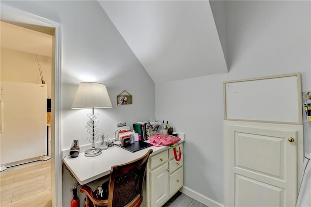 kitchen featuring baseboards, vaulted ceiling, light countertops, light wood-type flooring, and freestanding refrigerator