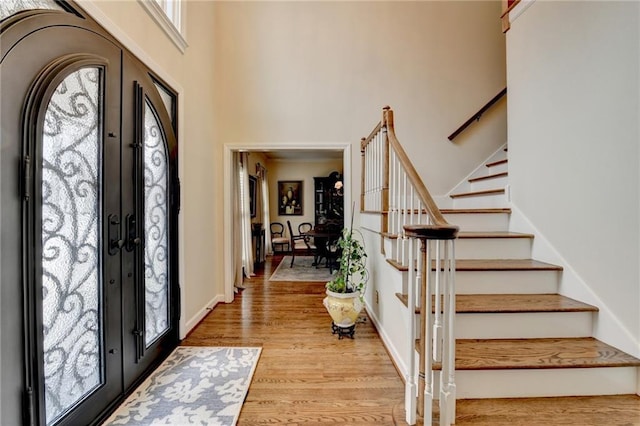 foyer featuring french doors, stairway, a towering ceiling, light wood-type flooring, and baseboards