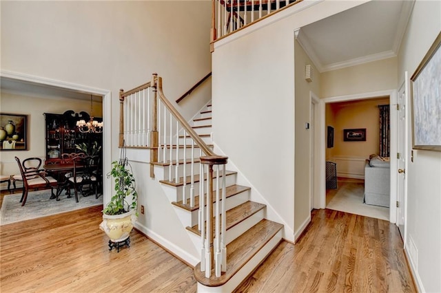 stairway with a notable chandelier, baseboards, ornamental molding, and wood finished floors