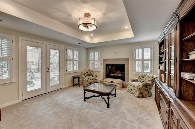 living room with baseboards, a premium fireplace, carpet, a tray ceiling, and french doors