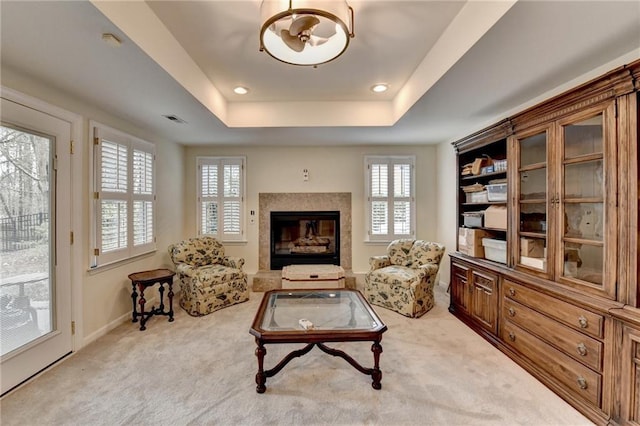 sitting room with baseboards, visible vents, a premium fireplace, a tray ceiling, and carpet flooring