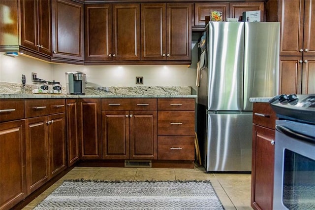 kitchen featuring appliances with stainless steel finishes, light tile patterned floors, light stone countertops, and dark brown cabinetry