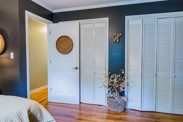 bedroom featuring crown molding, wood finished floors, two closets, and baseboards