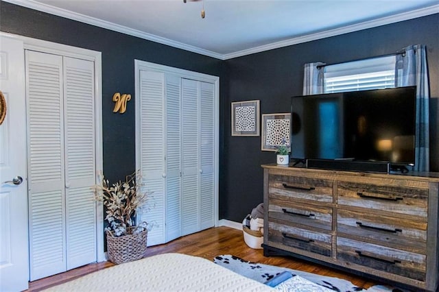 bedroom with multiple closets, wood finished floors, crown molding, and baseboards