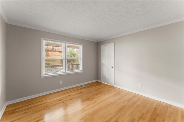 empty room featuring wood-type flooring, a textured ceiling, and ornamental molding