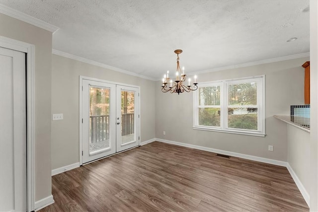 unfurnished dining area featuring french doors, a textured ceiling, crown molding, a chandelier, and dark hardwood / wood-style floors