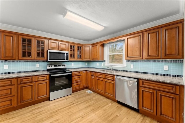 kitchen featuring sink, light stone counters, light hardwood / wood-style flooring, crown molding, and appliances with stainless steel finishes