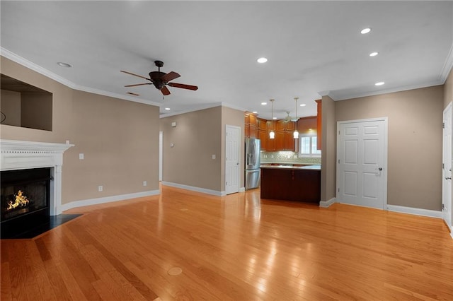 unfurnished living room with ceiling fan, ornamental molding, and light hardwood / wood-style flooring