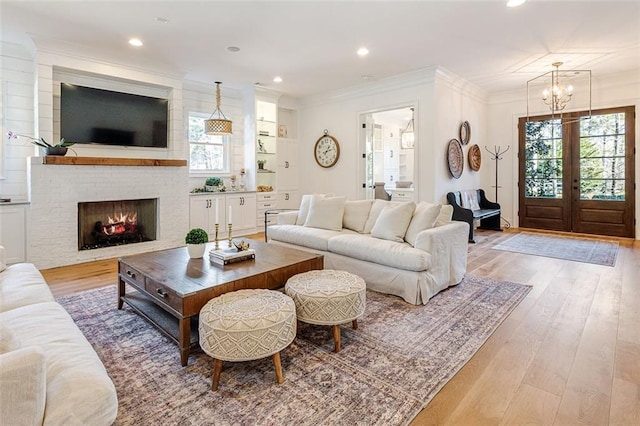 living room with a healthy amount of sunlight, ornamental molding, a brick fireplace, and light hardwood / wood-style flooring