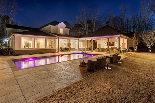 pool at twilight with ceiling fan, an outdoor kitchen, and a patio area