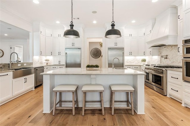 kitchen featuring decorative light fixtures, high quality appliances, sink, custom range hood, and a center island with sink