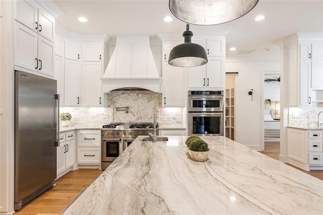 kitchen with high quality appliances, premium range hood, white cabinets, and decorative light fixtures