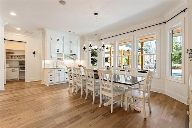 dining area with sink, ornamental molding, a notable chandelier, light hardwood / wood-style floors, and a barn door