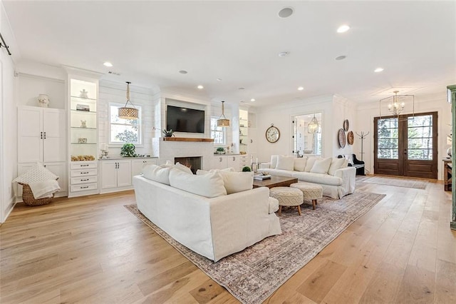 living room featuring french doors, ornamental molding, light hardwood / wood-style floors, and a brick fireplace