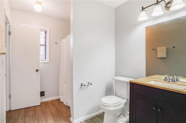 bathroom featuring visible vents, toilet, vanity, wood finished floors, and baseboards