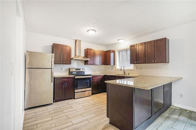 kitchen featuring freestanding refrigerator, a sink, wall chimney range hood, a peninsula, and stainless steel electric range