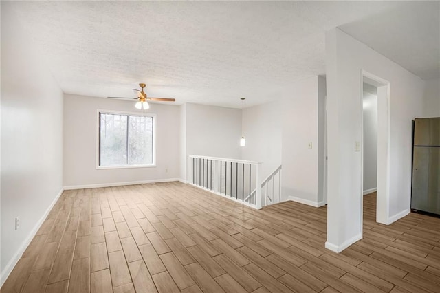 unfurnished room with ceiling fan, a textured ceiling, baseboards, and wood finished floors