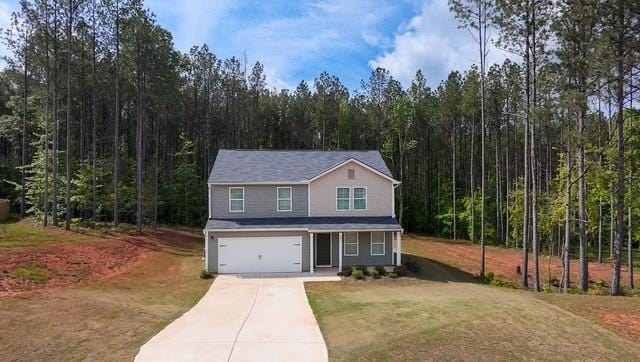 traditional-style home with an attached garage, a front lawn, concrete driveway, a forest view, and covered porch